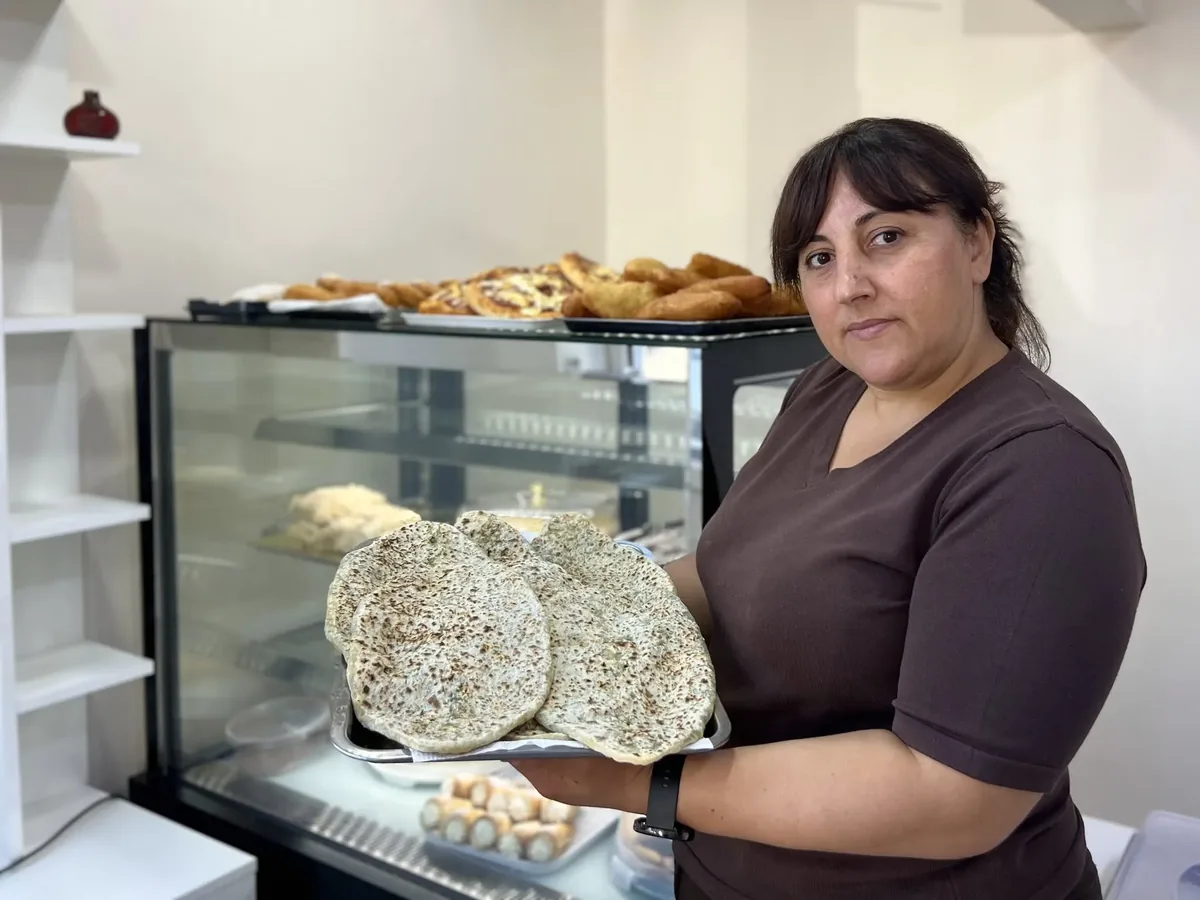 Lusine, a baker displaced from Artsakh, holding a tray of freshly baked zhengyalov hats in her bakery in Armenia