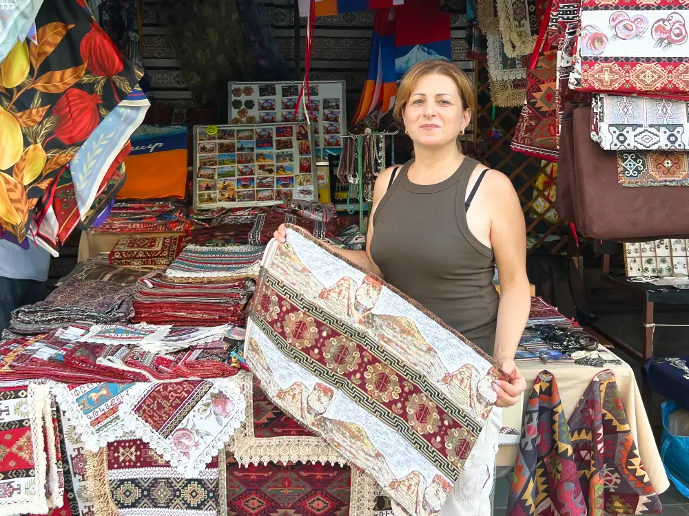 Liana, a refugee artisan from Artsakh, showing her handmade Armenian tablecloths at Yerevan's Vernissage market